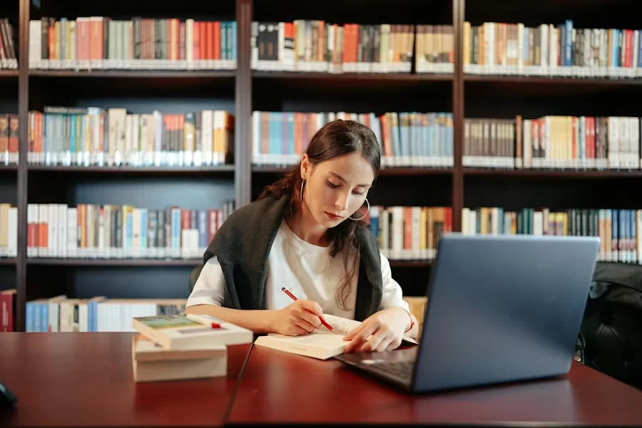 A student taking notes on a laptop in a library — studying in Portugal and the D4 visa
